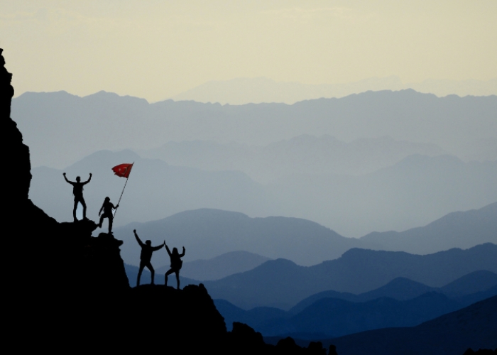 Image of a group of people climbing a mountain and holding a flag